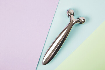 Steel face roller on the multicolor background. Flat lay. Trendy beauty tool for home skincare. Flat lay. Copy space for your text.