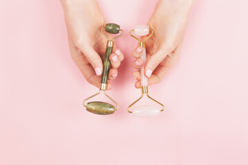 Jade roller in pink in woman hands with perfect manicure. Green and pink gua sha tools for skin beauty.
