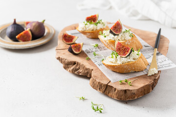 Bruschettas with figs and cheese on wooden board on white background. Side view, copy space for text, product place. Menu, recipe, banner design. Italian cuisine