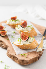 Fresh bread with figs, ricotta, honey and microgreen on a wooden cutting board on white background. Italian Bruschettas with figs. Close up, side view. Cookbook recipe, menu.
