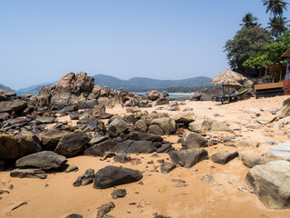 Fototapeta na wymiar Rocky coast of the Indian ocean with thatched sheds and sunbeds in Goa, India