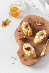 Sandwiches with ricotta, fresh figs, microgreen and honey on rustic wooden board over white backdrop, top view. Italian bruschetta recipe, menu. Healthy breakfast
