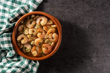 Garlic prawns in crockpot on black slate background. Top view. Copy space