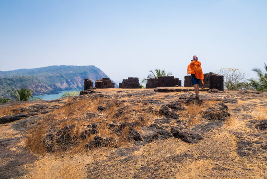 The photographer takes a picture of the remains of the fortress of Cabo de Rama in India on a blue background of sky, sea and mountains