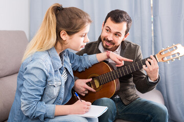 Young guitar tutor explaining basics to his female client at home