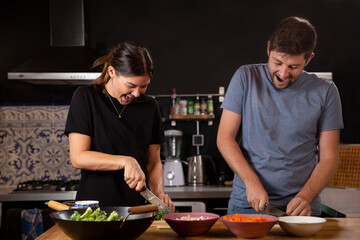 Young caucasian couple cutting vegetables and cooking asian food smiling