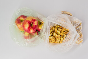 Two transparent plastic crumpled cellophane bags with groups of ripe red apples and yellow dried slices of dry apples on white backdrop. Top view. Ecology concept