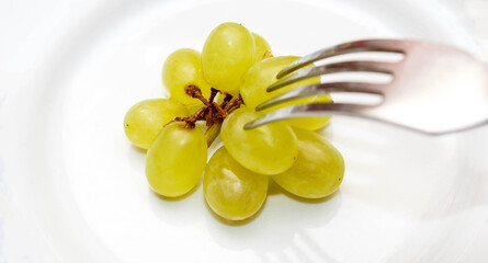Green grapes on a plate, which is impaled on a fork. The concept of healthy and proper nutrition.