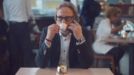 Senior businessman on coffee break in restaurant having phone conversation with business partner
