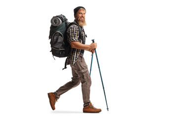 Full length profile shot of a bearded guy hiker with a backpack and hiking poles walking - obrazy, fototapety, plakaty