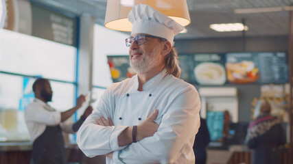 Portrait of happy mature chef in uniform standing in modern bistro restaurant