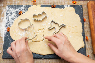 Making cookies for Halloween. A woman cuts out cookies from the dough in the form of pumpkin, cat, Ghost and bat