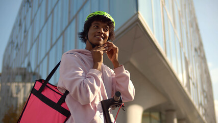 African delivery man putting on helmet riding electric kick scooter carrying thermal box © nimito