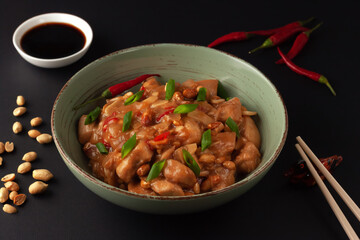 Kung Bao chicken on a black background. A Chinese dish with chicken, chili, peanuts, sauces and onions.