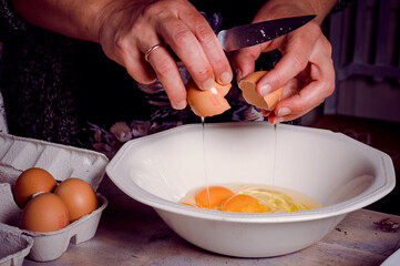 Breaking and pouring raw eggs into a white bowl
