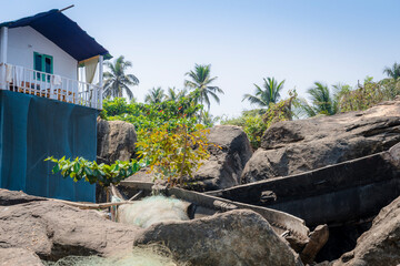 PALOLEM, GOA, INDIA - MARCH 19, 2019: View of old broken wooden boats and fishing nets on a rocky slope next to a village house in Palolem, Goa, India