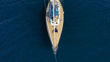Aerial drone top down photo of beautiful wooden sailboat anchored in Aegean deep blue sea near island of Santorini, Cyclades, Greece