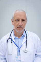 Portrait of senior male doctor against grey background