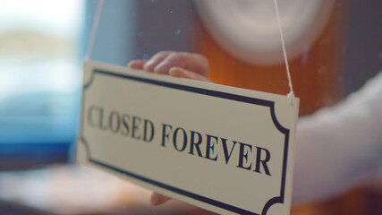 Close up of human hand hanging closed forever sign on glass door of cafe or store