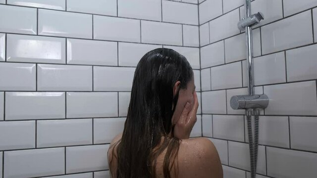 Sad depressed girl crying in shower under running water back view close up. Woman in bathroom being unhappy without clothes. Dramatic concept of woman sadness. Slow motion. 4k footage