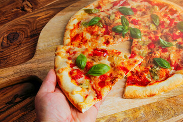 Freshly baked homemade tuna pizza sprinkled with basil in a man's hand. Old wood as a background . Copy space for text or description.
