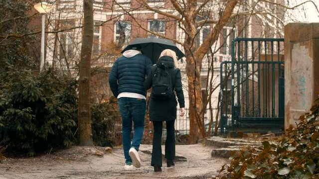 Couple walking through Vondelpark in Amsterdam with umbrella