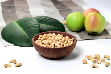 Cashew nuts in a wooden bowl, green leaves and apples isolated on white background. Clipping path stil photo
