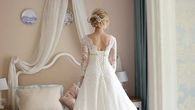 close - up portrait of the bride, rear view. Bride in a chic wedding dress in a home interior. The bride is standing by the big bed with her back to the camera. Wedding concept