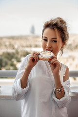 Fototapeta na wymiar young beautiful Asian girl in beige lace shorts,white shirt eating dessert, pie on the balcony. selective focus. small focus area