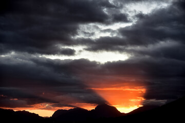 Silhouetted mountains and fiery sunset against dark clouds