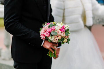 Wedding bouquet of roses in the hands of the groom in a suit