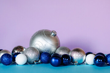 Christmas balls in blue, white and silver colors are arranged in a row on a turquoise and pink background.