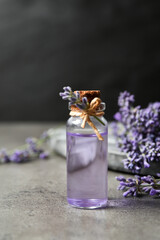 Bottle of essential oil and lavender flowers on grey stone table