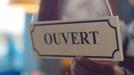 Close up of waiter turning french open sign ouvert hanging on glass door