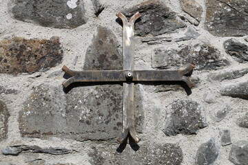 A closeup view of a  structural wall anchor plate in the form of a cross supporting an old stone wall.