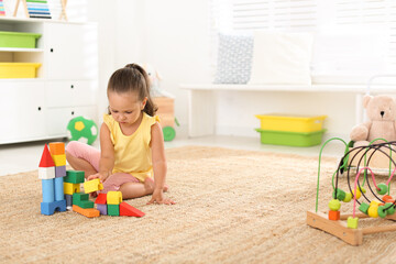 Cute little girl playing with colorful blocks on floor indoors, space for text. Educational toy