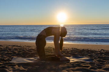 Fototapeta na wymiar young caucasian woman doing stretches and yoga exercises on the beach on sun rising.