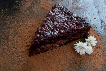 Chocolate-flower slice of cake with cocoa on a black stone board. Yummy.