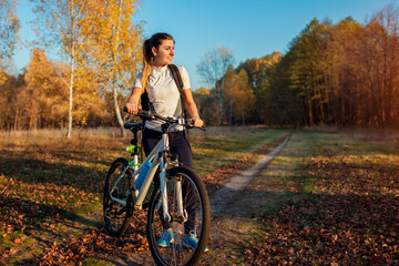 Plakat Riding bicycle in autumn forest. Young woman having rest after workout on bike enjoying nature. Healthy lifestyle