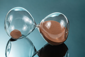 Hourglass with brown quartz sand lying on the mirror surface