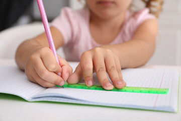 Little girl drawing with ruler and pencil at table, closeup. Doing homework