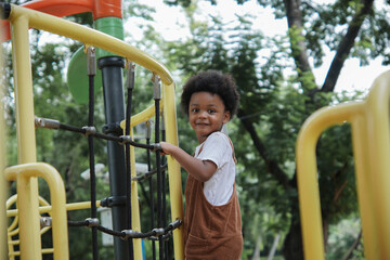 Fototapeta na wymiar Active African little boy afro hair enjoy playing outdoors, 3 Years kid having fun climbing rope on playground in the park on a sunny day, side view