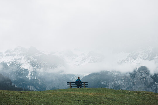 man sitting on bench looking at snow covered mountains panorama - Powered by Adobe
