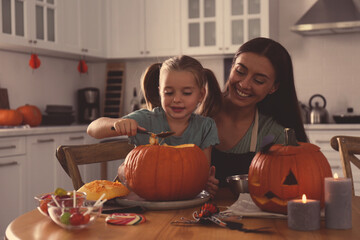 Mother and daughter making pumpkin jack o'lantern at table in kitchen. Halloween celebration