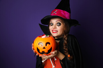 Cute little girl with pumpkin candy bucket wearing Halloween costume on purple background