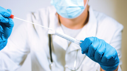 Doctor holding coronavirus swab test sample in a vial with gloves and face mask at laboratory. Close up