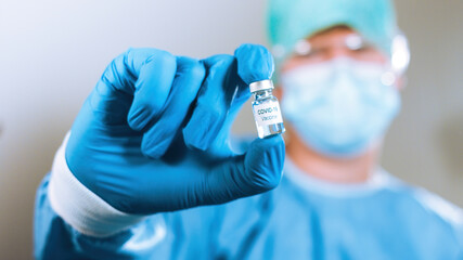 Virologist doctor with coronavirus vaccine in a medical vial. Close up