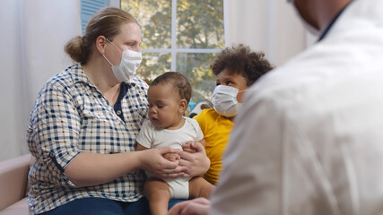 Doctor visiting multiethnic family with little children wearing protective mask - Powered by Adobe
