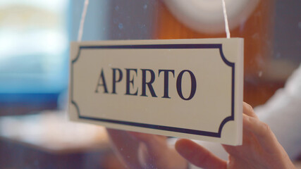 Close up of staff turning aperto sign hanging on glass door in italian restaurant.