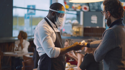 African-american staff checking body temperature of customer using thermal scanner in cafe